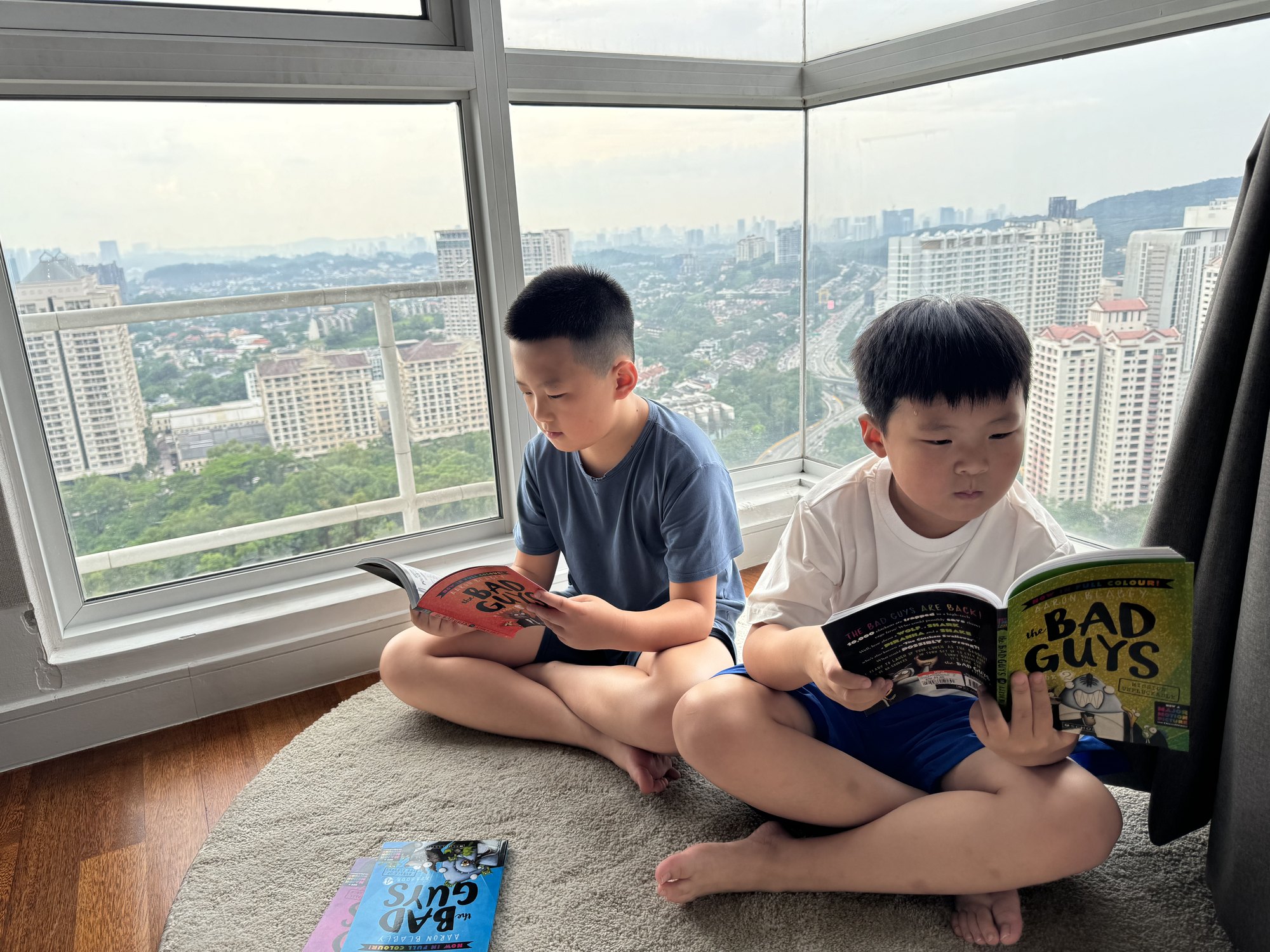 两个孩子坐在窗边的地毯上看书