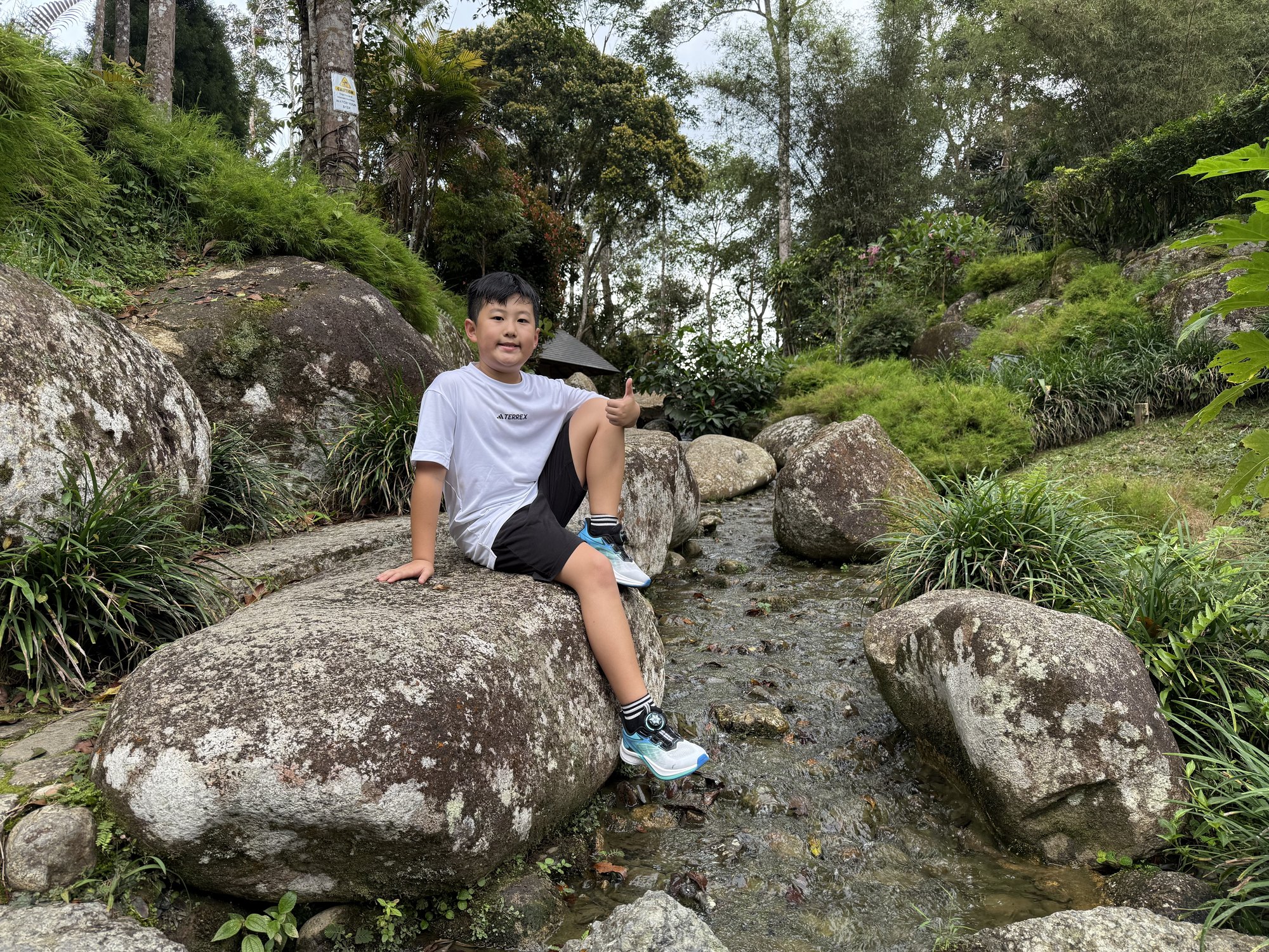 一个孩子坐在溪流旁的大石头上