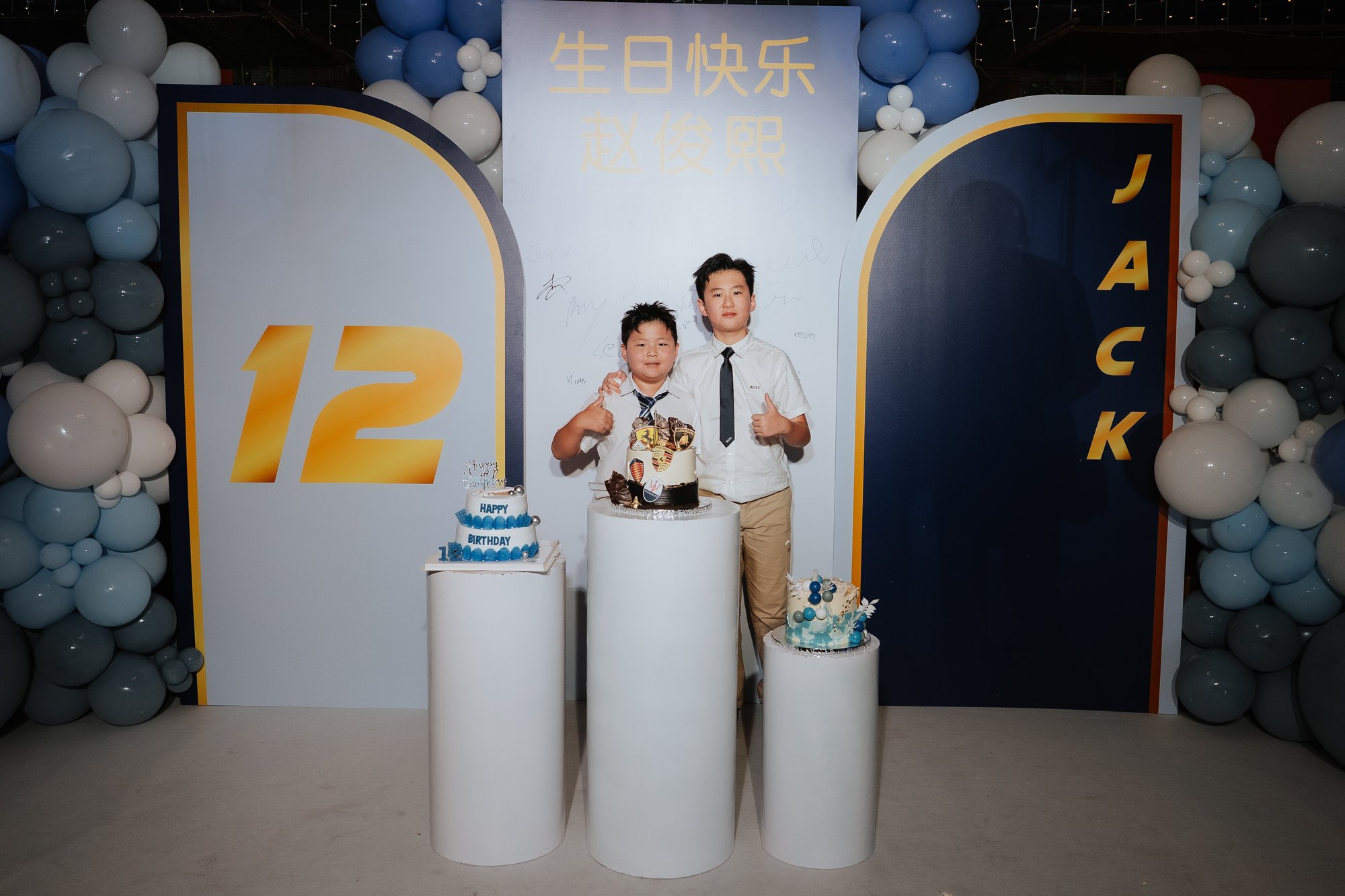 两个孩子站在生日蛋糕和蓝色气球前